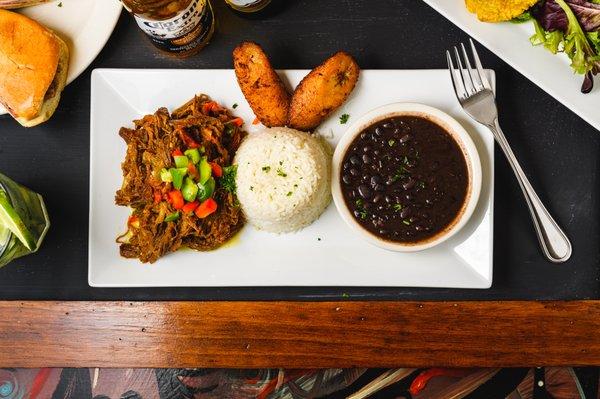 Heartwarming Ropa Vieja (Shredded Beef) in a Cuban creole sauce, with sweet plantains, white rice and black beans.