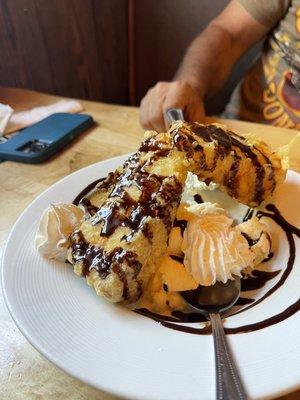 Two slice Deep fried cheesecake with vanilla ice cream and chocolate glaze and whip cream.