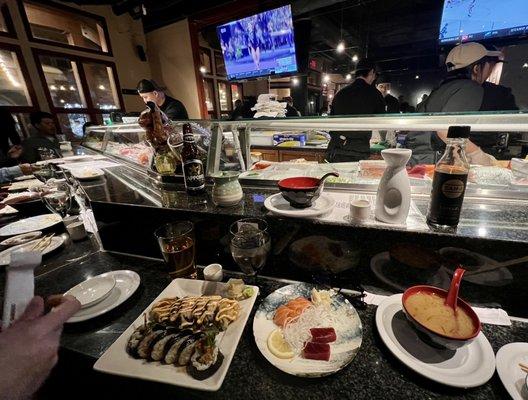 Seating at sushi bar with rolls, sashimi, miso soup,  Saki and Sapporo ~ with Tamari GF soy sauce for all off us Celiac/GF guests.