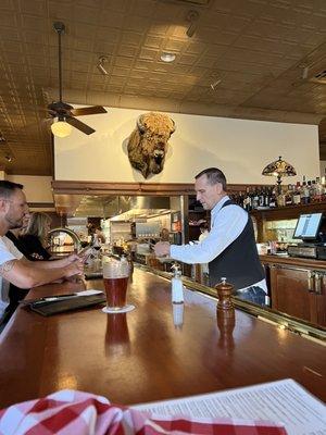 The bartender is watched over by a huge bison head.