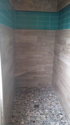 Customer Shower Wood look porcelain ran horizontal with a brick style glass in a running niche and a river rock floor