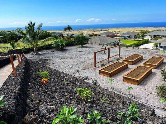 Rock retaining wall with a concrete ramp, custom planter boxes, the living fence with lilikoi vine, and the upgraded irrigation system