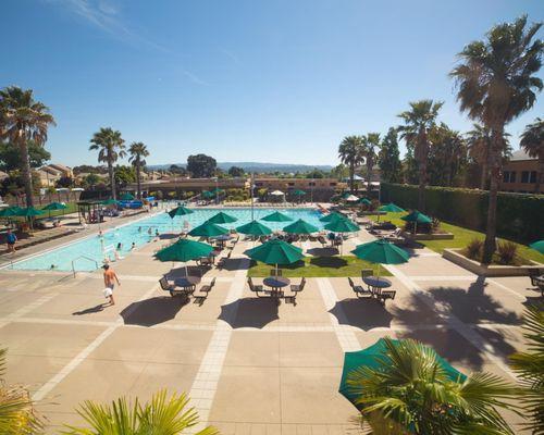 Heated outdoor pool area for open swim, lap swim, and swim team with lounge tables & chairs, outdoor fitness park, and cycling