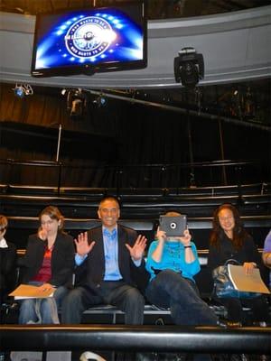 NYC Brainiacs forming the audience and beneath a monitor identifying the show, "Who wants to be a millionaire?"