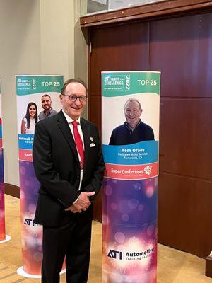 Tom Grady (owner) at ATI Super Conference 2023  and standing next to his Top 25 ATI Shop photo