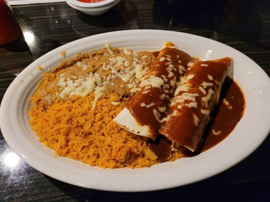 Two chicken burritos with enchilada sauce and melted cheese, rice and beans.