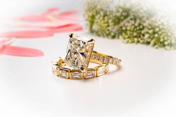 A 4.37 carat radiant cut diamond in a yellow gold ring setting paired with all bezel set emerald cut diamond band.