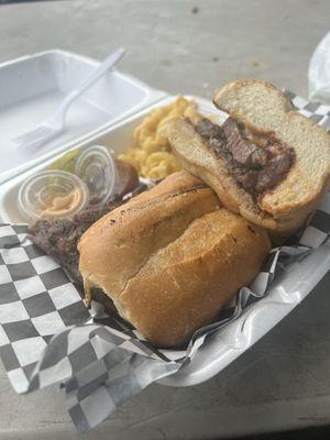 A ribeye steak sandwich w grilled onions and a side of mac n cheese. Made to perfection