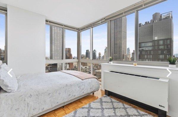 Second space behind bookshelf with corner windows and a full bed