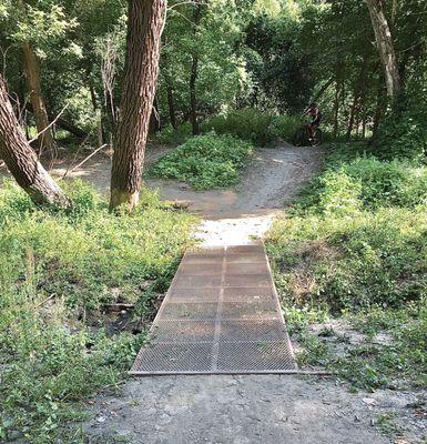 A cyclist begins their descent to a foot bridge over a small creek.