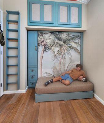 One side of the room features a hidden Murphy Bed with art-a palm tree print. Loung seating when the bed isn't in use, and storage.