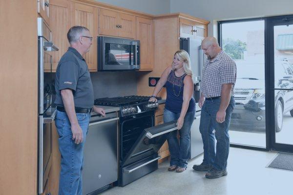 A showroom featuring a variety of high-end kitchen appliances. A sales associate is demonstrating the features of an oven to ...