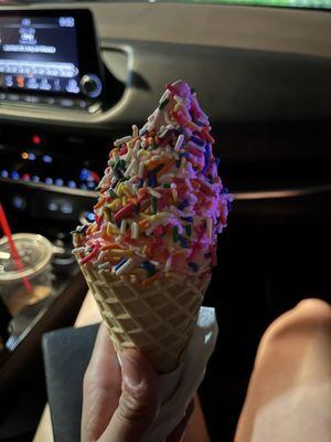 strawberry ice cream with rainbow sprinkles in a waffle cone.