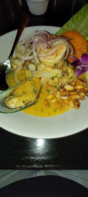 Seafood aji Amarillo ceviche. Shrimp, mussels, fish, calamari, Peruvian corn 2 ways, sweet potato slice, red onions, in a citrus sauce.