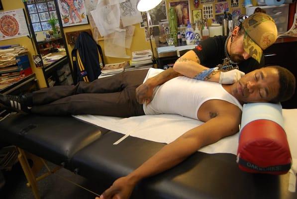 tattooer, Viktor Macias putting finishing touches on  "swallow" neck tattoo on client, Kwote.