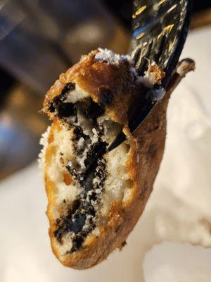 Close-up of a black plastic fork holding a fried Oreo.