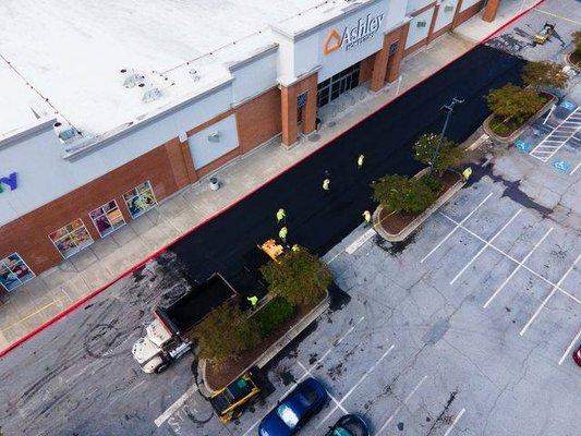 Aerial shot of Blackjack Paving contractors laying fresh asphalt in a parking lot outside of an Ashley HomeStore