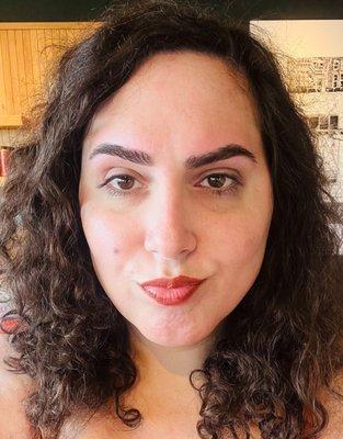 A close up of a woman (Crystal) in her 30's - with dark brown curly hair, red-orange lipstick, and freshly threaded brows.