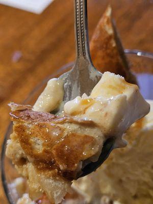 A spoonful of the Flash-Fried Banana Cheesecake in a glass bowl with vanilla ice cream and drizzled with caramel sauce.