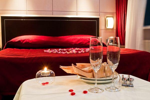 A bedroom proposal covered with rose petals, candles, and champagne.