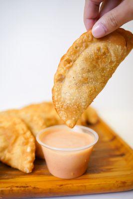 An empanada being dip with tropical sauce