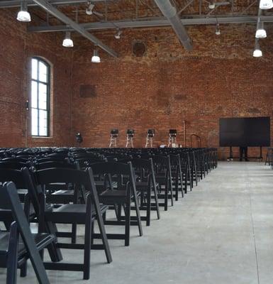 Loray Mill Event Hall is 3,023 square feet of original brick, a high bay ceiling, and antique windows. It can fit 420 people maximum.