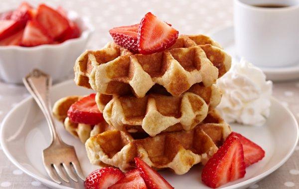 Warm waffles served with a side of fresh strawberries and whipped cream