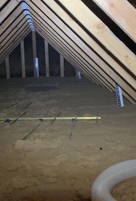 A typical older attic with barely 4" of 30 year old insulation.  Rulers help guide our technician and assure you of our work quality!