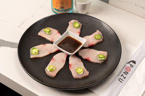 Our Hamachi Jalapeño - Delicately sliced yellowtail topped with garlic, cilantro, and jalapeño, served with yuzu dressing.