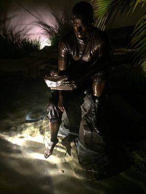 A bronze statue of Ernie Pinamonti by a reflecting pond reading a letter from home.