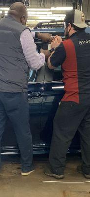 A mechanic and my salesperson prying open my new car that they locked my keys in.