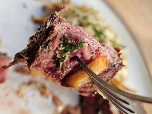 Close-up of a piece of Hanger Steak on a fork with a French Fries.