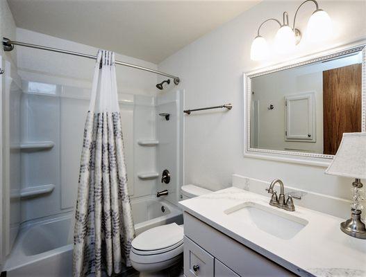 Complete bathroom remodel with new tub enclosure, lighting, vanity, countertop, and tile floor.