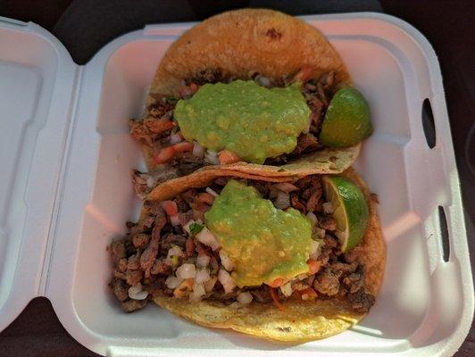 Two tacos: carnitas (top) and carne asada (bottom), both served with a dollop of guacamole and light pico de gallo.