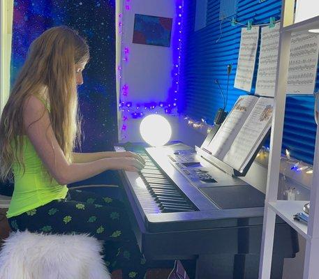 My daughter playing the piano at home, where she has her "phone-call" piano lessons with Irwin.