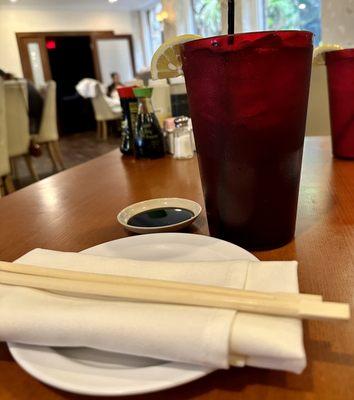 Large sweet tea with condiments in the background and cloth napkin with wooden chopsticks.