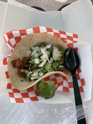 Taco al pastor on a corn tortilla with cilantro, tired onion and salsa verde cremosa. Lime on the side.