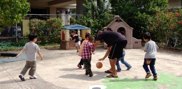 The boys enjoy basketball with their teacher during playground time.