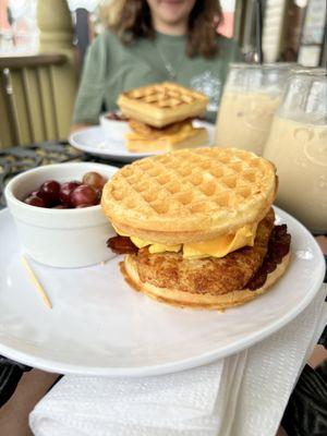 Waffle sandwich with bacon, egg, cheese, and a hashbrown patty. A side of grapes and a brown sugar cinnamon almond milk latte.