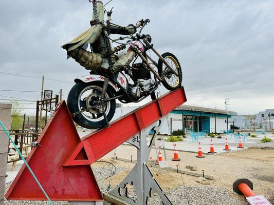 A steampunk knight on a motorcycle atop a giant red arrow pointing to the entrance of Rickety Cricket Brewery (Dirty Duh is found inside).