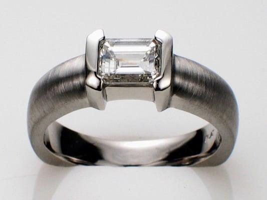 Platinum ring with Emerald-cut diamond set in bracket-style semi-bezel. shank: brushed; setting: polished.