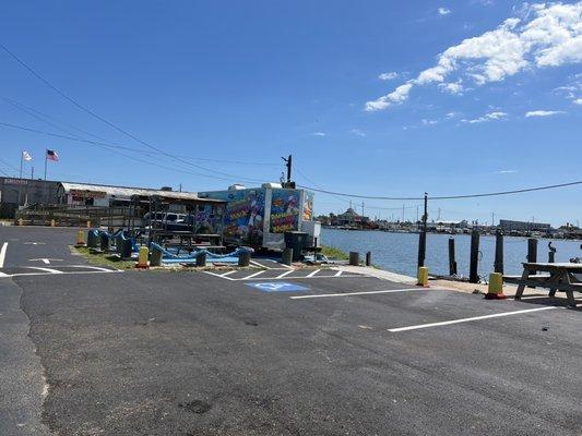 Covered tables and benches by food truck and table and bench to far right by the waterfront.