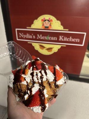 Buñuelos topped with whipped cream, strawberries, and chocolate drizzle