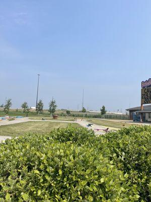 Outside area. There is a race track with trikes, and beyond there in the distance there is a pirate themed playground and splash pad areas.