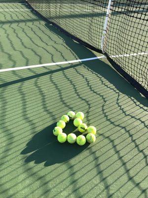 Love heart shape made of tennis balls on court with net shadow