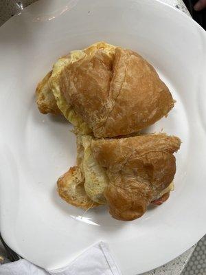 Breakfast sandwich, with ham, egg, and cheese on croissant, cut in half.