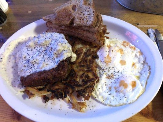 Chicken fried steak with hash browns, eggs and toast.