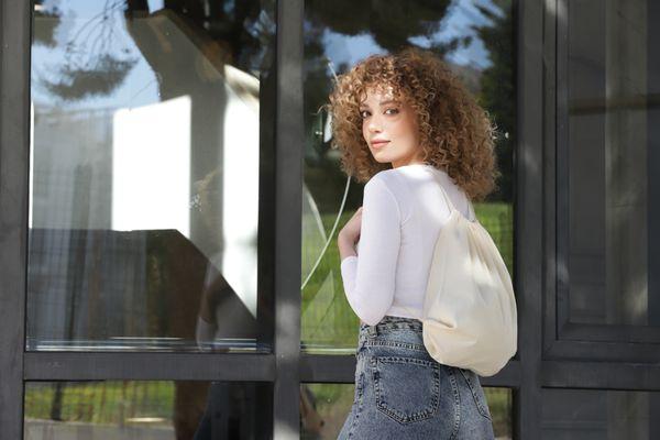 Stunning image of a model elegantly displaying a natural drawstring tote. Its design, both chic and functional, stands out as she effortless