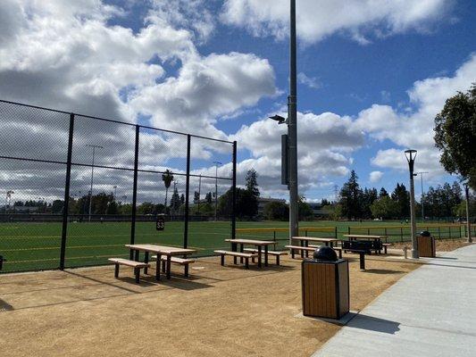 Picnic tables outside the play area , next to new field