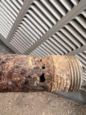 Corroded 2 inch black iron natural gas pipe full of holes going from gas meter thru sleeve in house wall into crawl space